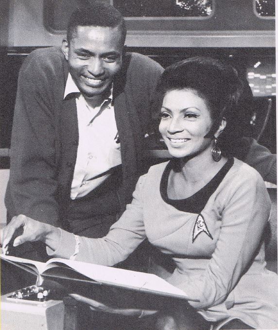 A photo from the Starlog article Charlie Washburn wrote. In the photo, Washburn leans over Nichelle Nichols, sitting in the captain's chair, as she reviews a script. 