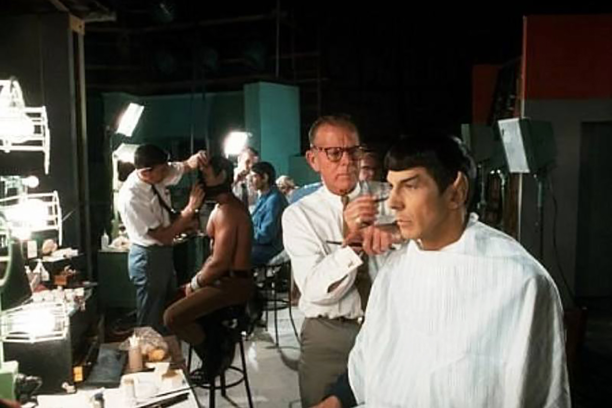 Make-up man Fred Philips at work on Spock, in preparation for filming Amok Time. The photo is in colour and shows Phillips, Leonard Nimoy, plus other make-up artists and actors in the background.