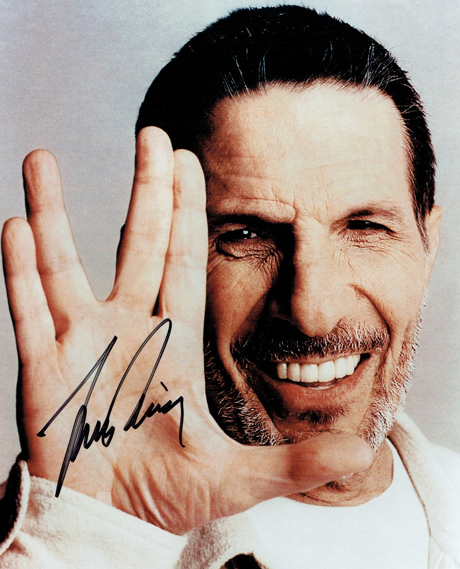 An 8x10 of an older Leonard Nimoy, not in character, holding his hand in the traditional Vulcan greeting gesture. It is autographed by Nimoy.