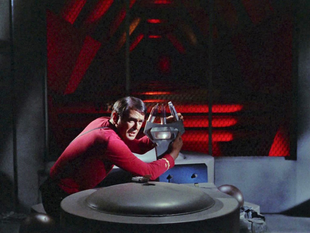Scotty is seen crouching beside the back wall of Engineering, holding a trident scanner. 