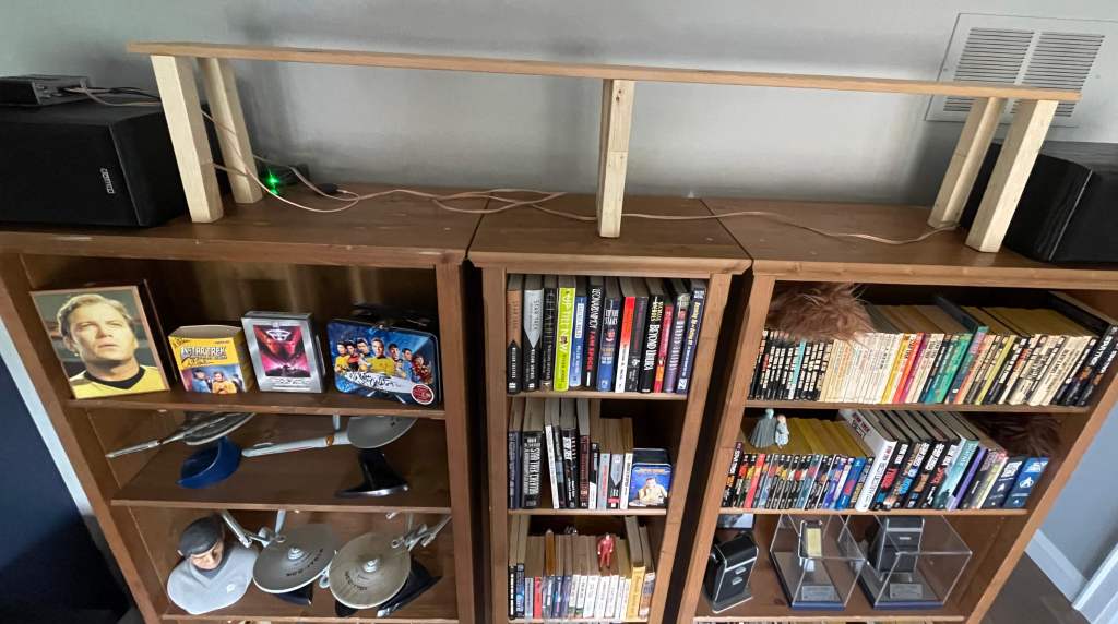 The wood shelf, sitting by itself on top of bookcases. It is an inexpensive board with six square legs glued underneath.  